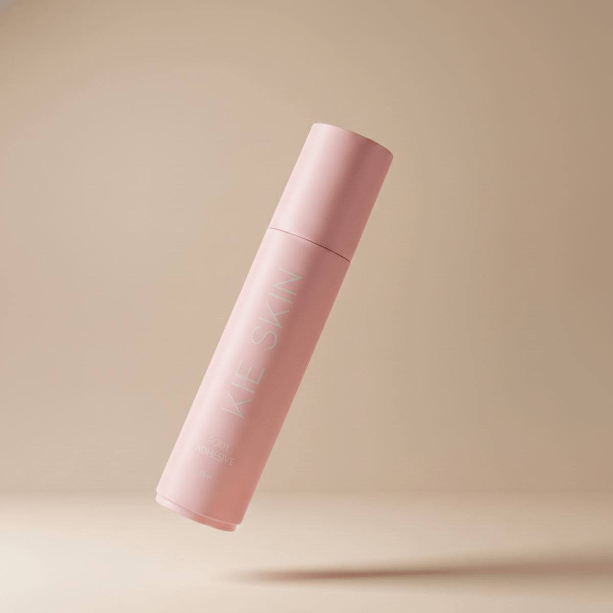 Kie Skin Body Adhesive pink roll-on bottle with cap on, floating against a beige background