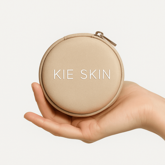 Hand holding the round beige Kie Skin travel pouch with zip closure